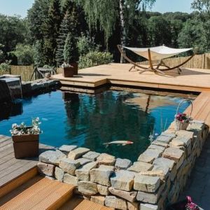 Auf diesem Bild ist ein von uns abgedichteter Koi Teich mit einer Steinmauer zusehen, rundherum ist eine Holzterrasse.