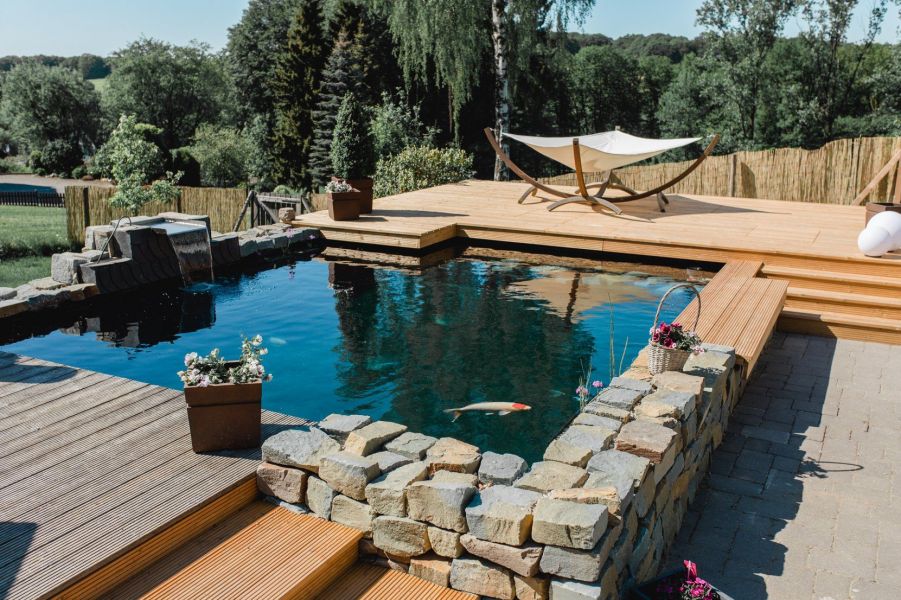 Auf diesem Bild ist ein von uns abgedichteter Koi Teich mit einer Steinmauer zusehen, rundherum ist eine Holzterrasse.